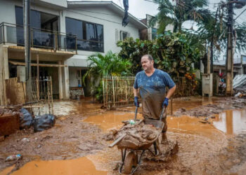 Homem com carrinho de mão em local alagado. (Divulgação)