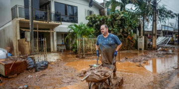 Homem com carrinho de mão em local alagado. (Divulgação)