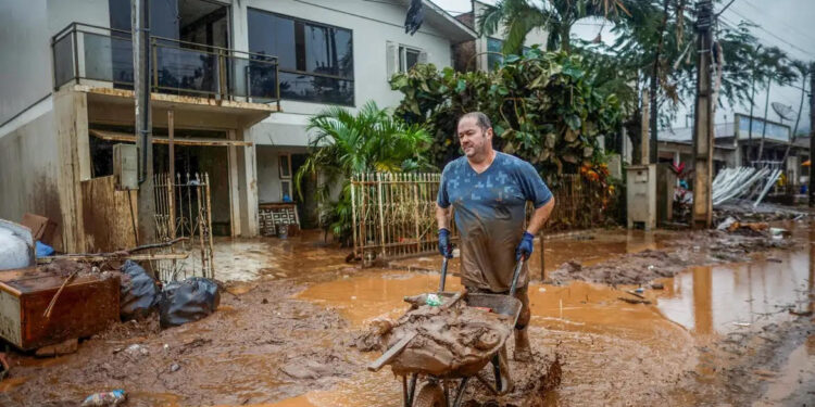 Homem com carrinho de mão em local alagado. (Divulgação)